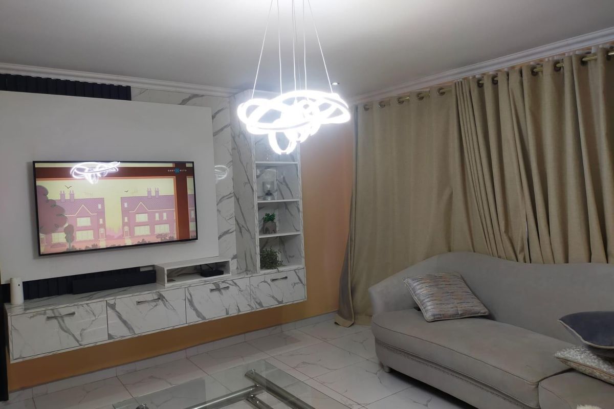 A modern living room featuring a custom built-in media unit with marble-effect finish, recessed shelving, and a contemporary statement pendant light.