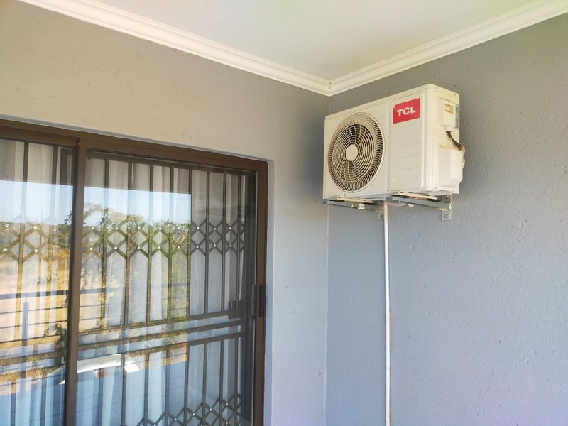 A covered patio area featuring a wall-mounted air conditioning condenser unit and a sliding glass door with a security gate.