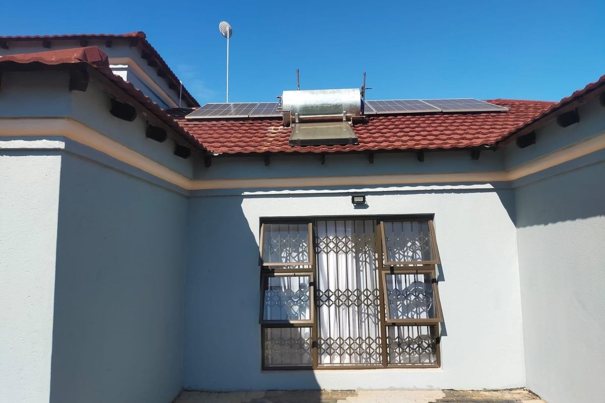 Rear exterior view of the property featuring a tiled roof, solar water heating system, solar panels, and a window with a security gate.