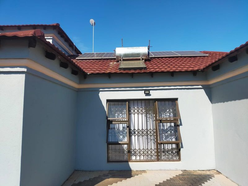 Rear exterior view of the property featuring a tiled roof, solar water heating system, solar panels, and a window with a security gate.