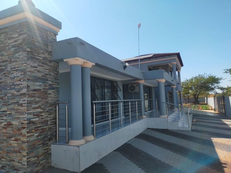 Front elevation of a modern house featuring stone cladding, decorative columns, a stainless steel balustrade, and a paved driveway.