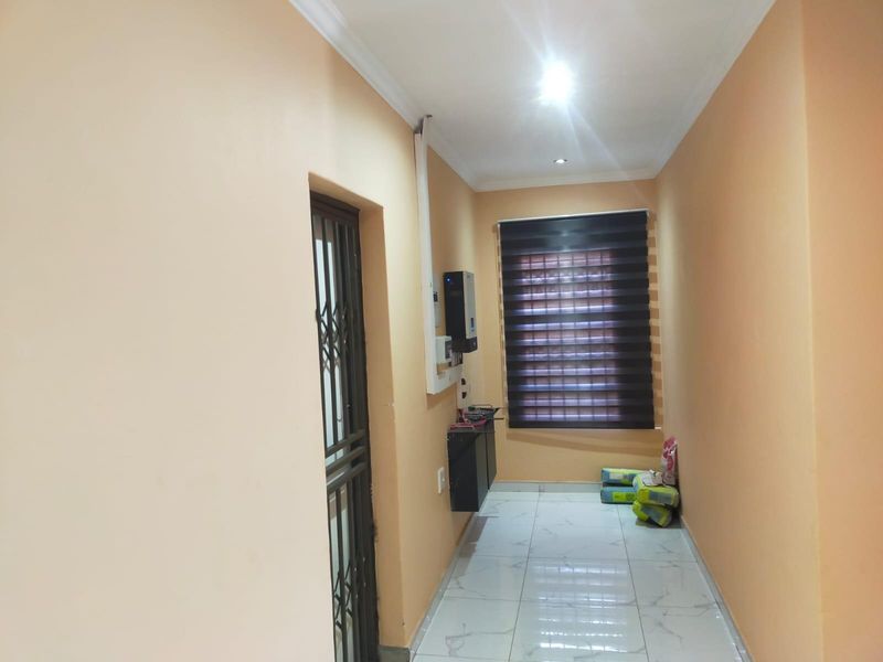 A clean, tiled hallway featuring a security gate, roller blind, and neutral wall finishes, providing a functional transition space within the home.