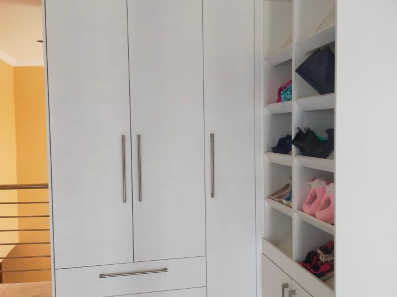 A bedroom featuring a modern white built-in wardrobe with integrated shelving and drawers, complemented by tiled flooring.