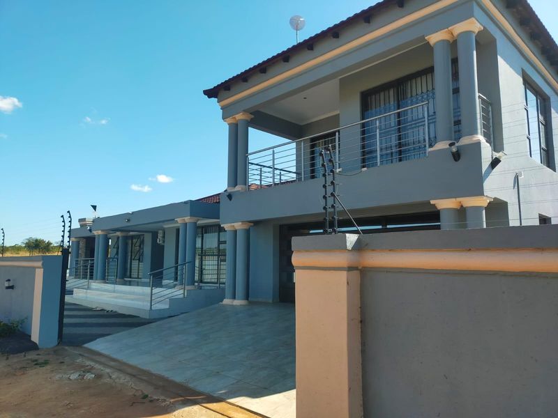 Modern double-story house exterior featuring a tiled driveway, balcony with stainless steel balustrades, and secure perimeter wall with electric fencing.