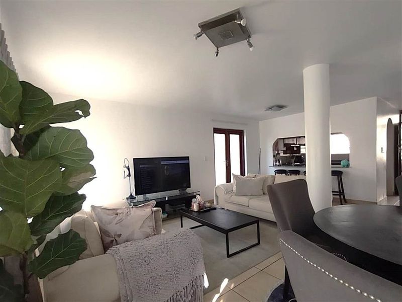 An open-plan living and dining area featuring tiled flooring, a structural column, and a breakfast bar connecting to the kitchen space.