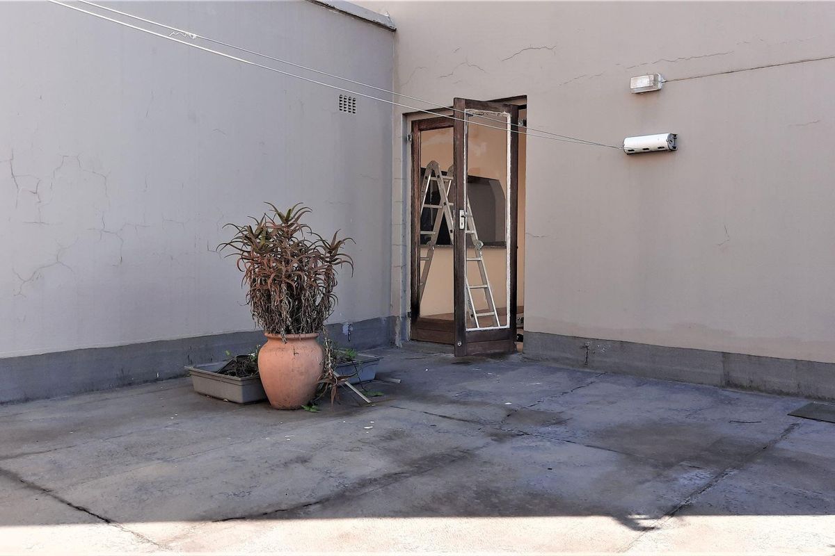 A rear exterior patio area featuring concrete flooring, a wall-mounted light, and a clothesline, showing signs of wear and requiring maintenance.