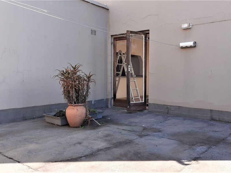 A rear exterior patio area featuring concrete flooring, a wall-mounted light, and a clothesline, showing signs of wear and requiring maintenance.