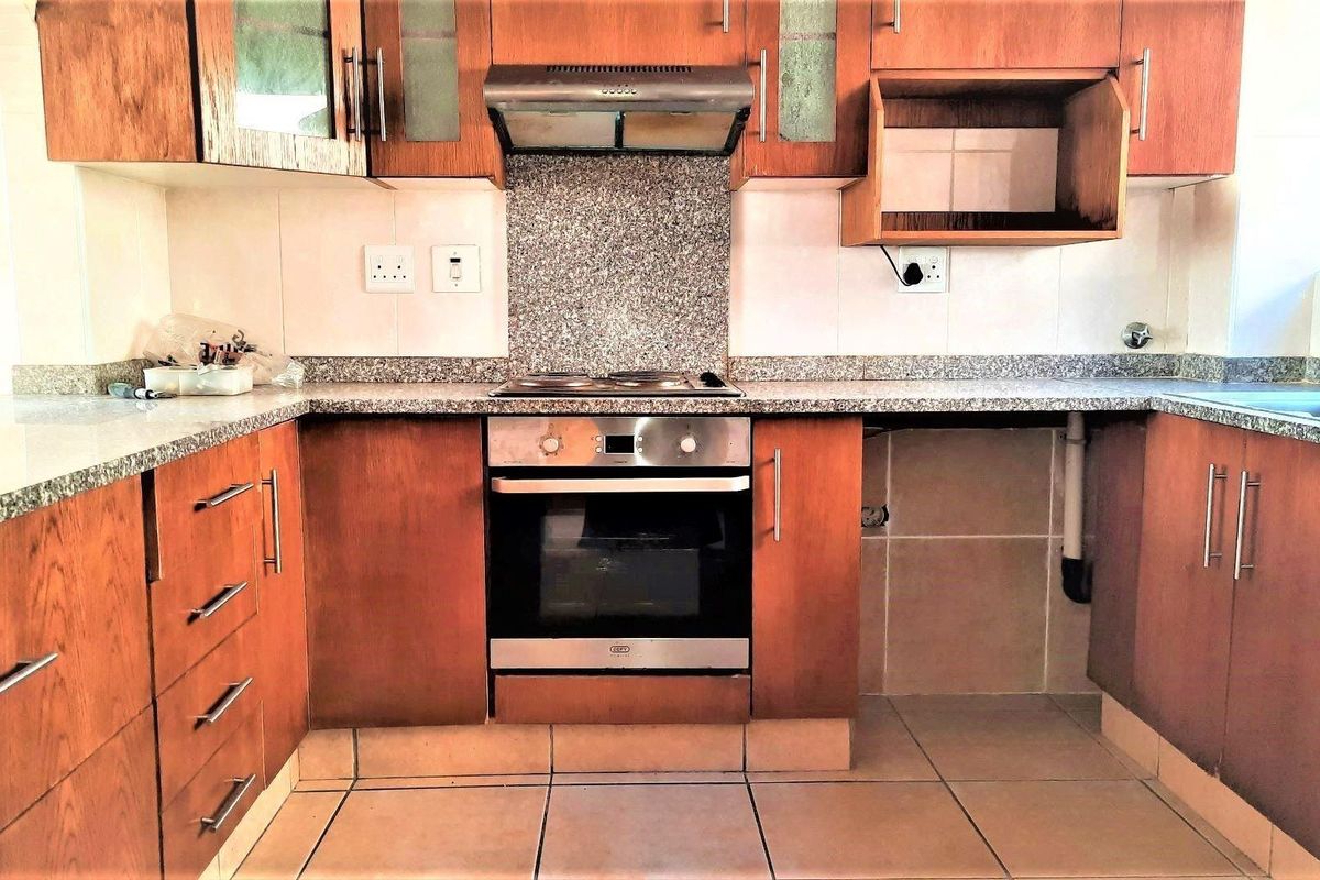 A functional kitchen featuring wooden cabinetry, granite countertops, a built-in oven with hob, and a tiled backsplash, offering a practical layout for daily use.