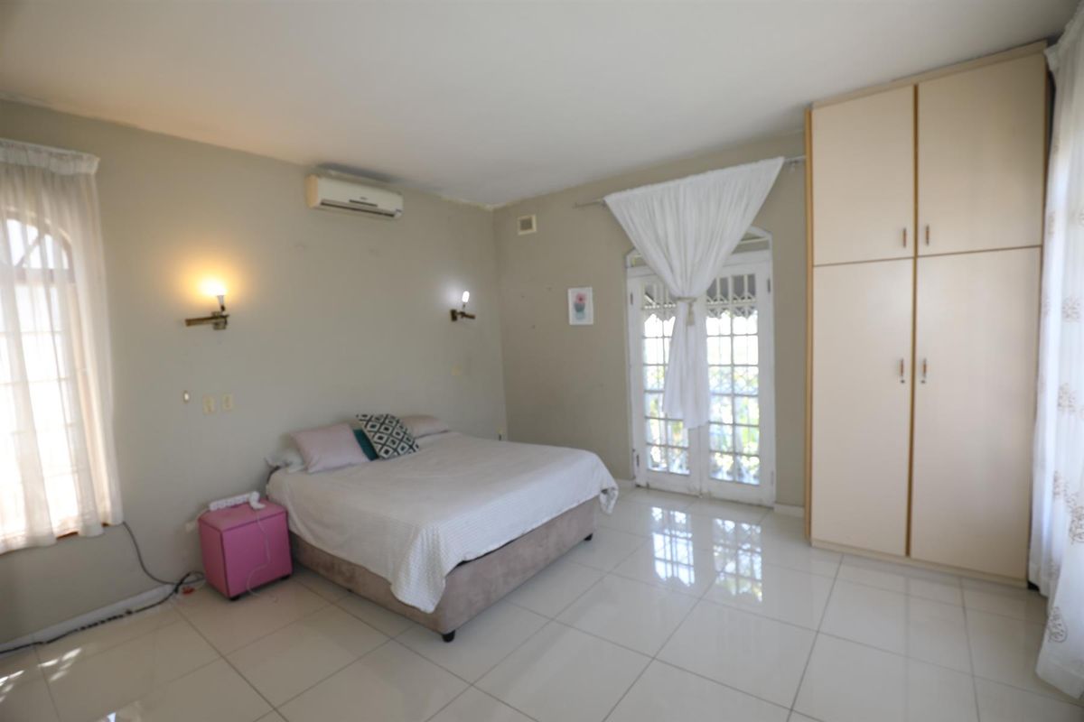 Spacious bedroom featuring tiled flooring, built-in cupboards, wall-mounted air conditioning unit, and French doors leading to the exterior.
