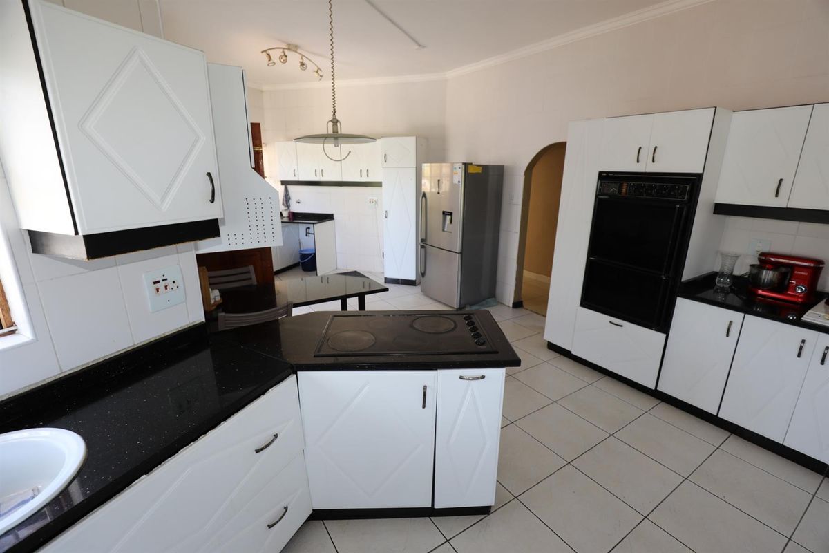 A functional kitchen featuring white cabinetry, black granite countertops, a built-in oven, and a central island with an integrated electric hob.