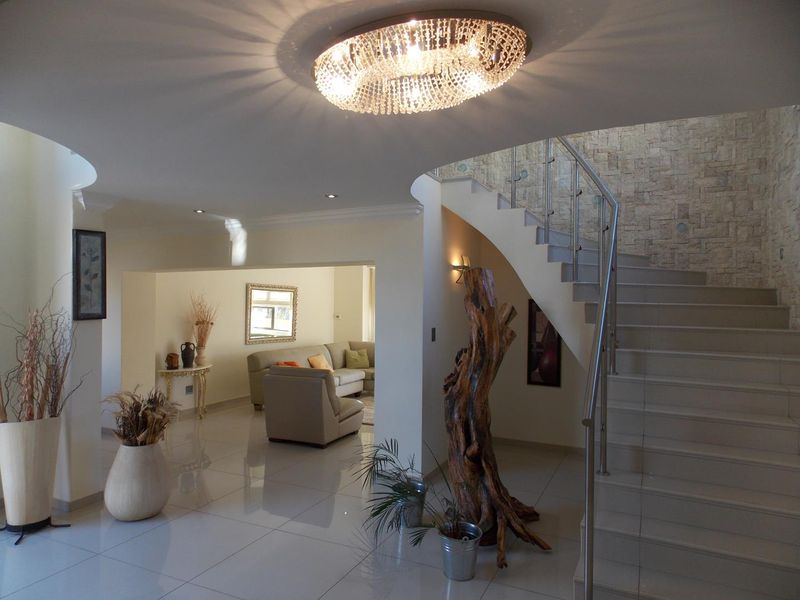 Spacious entrance hall featuring a grand curved staircase with glass balustrades, polished tile flooring, and a decorative crystal chandelier.