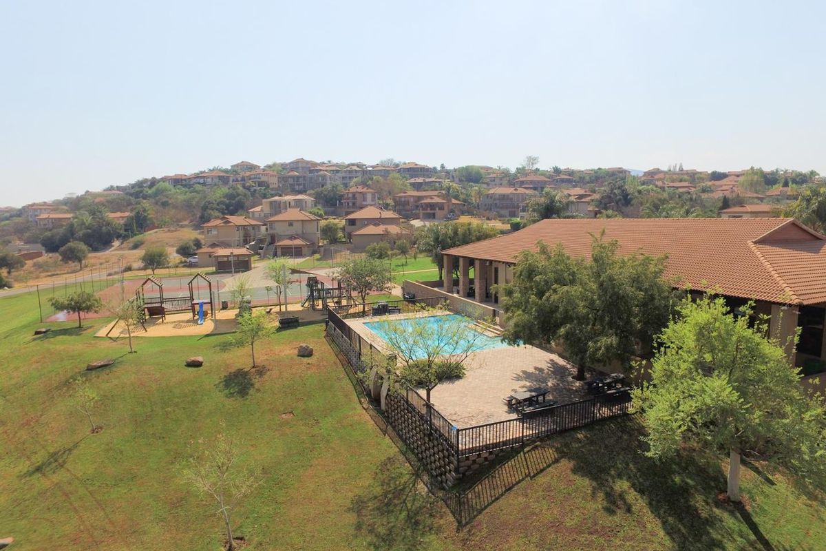 Aerial view of a residential estate featuring a communal swimming pool, paved patio area, and adjacent sports facility with a playground.
