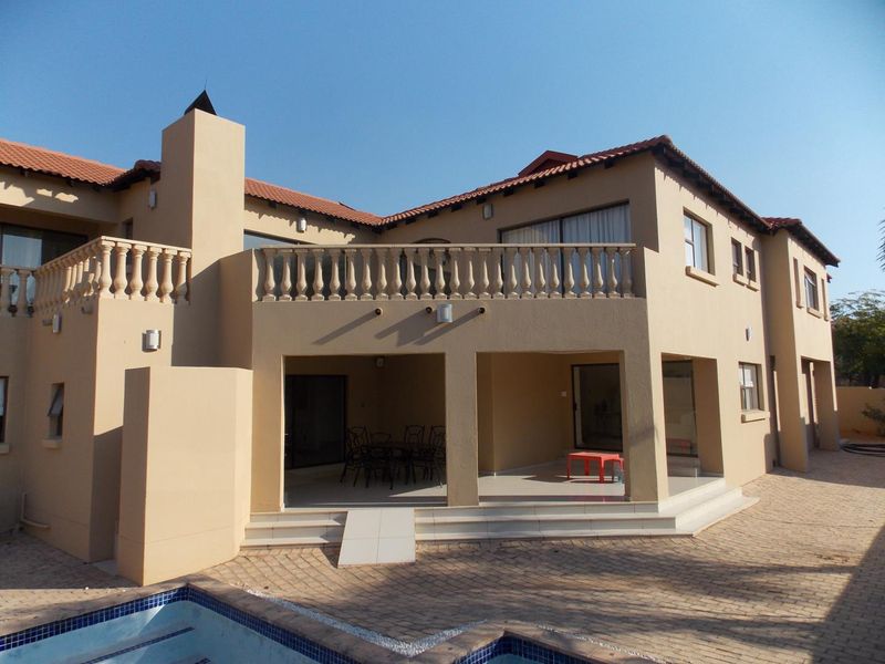 Rear view of a two-story house featuring a covered patio, upper-level balcony with balustrades, tiled roof, and an adjacent swimming pool.
