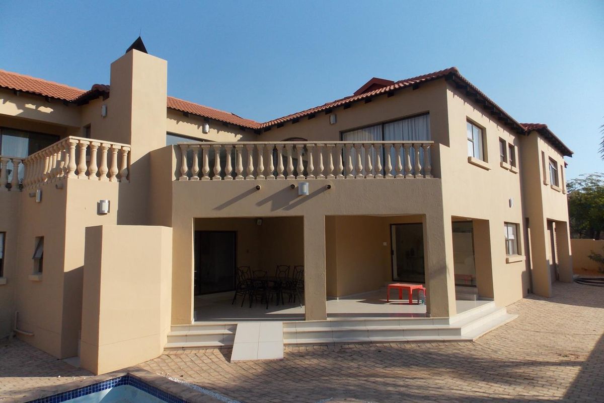 Rear view of a two-story house featuring a covered patio, upper-level balcony with balustrades, tiled roof, and an adjacent swimming pool.