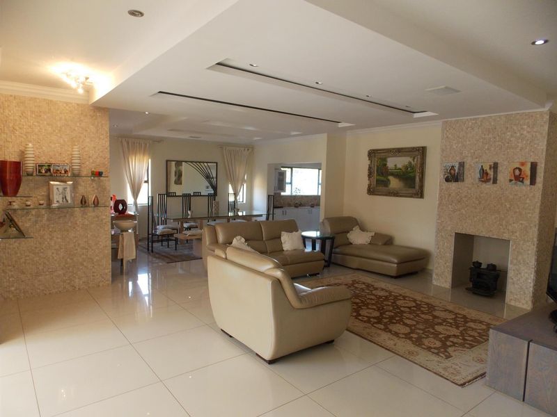 Spacious open-plan living and dining area featuring polished tile flooring, a built-in fireplace with mosaic tiling, and recessed ceiling lighting.