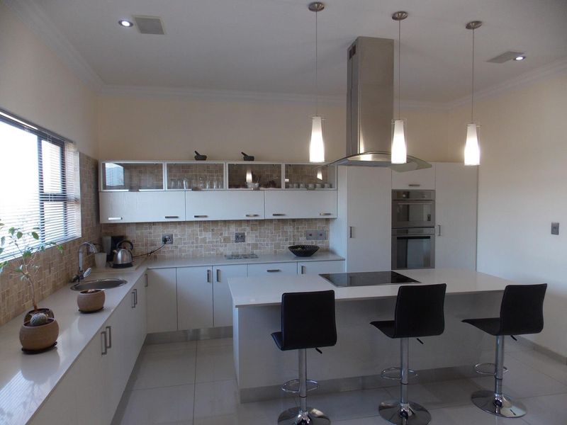 Modern kitchen featuring white cabinetry, stone countertops, a central island with a built-in cooktop, stainless steel extractor fan, and integrated wall ovens.
