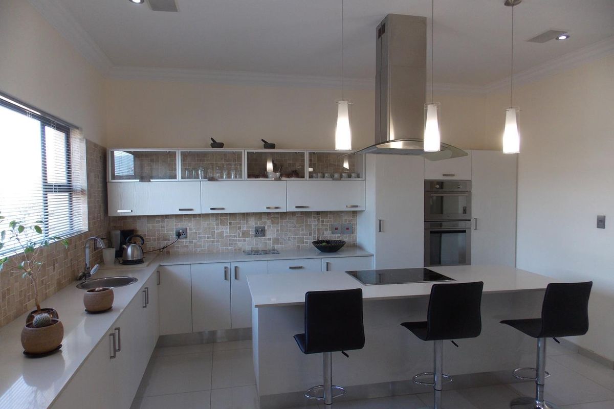 Modern kitchen featuring white cabinetry, stone countertops, a central island with a built-in cooktop, stainless steel extractor fan, and integrated wall ovens.