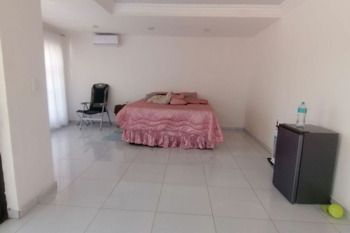 Spacious bedroom featuring large format floor tiles, recessed ceiling lighting, and a wall-mounted air conditioning unit.