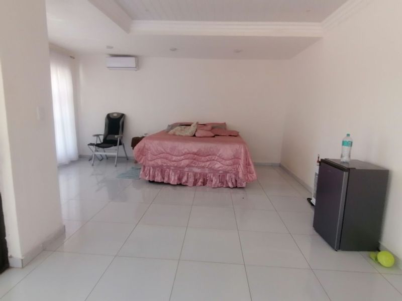 Spacious bedroom featuring large format floor tiles, recessed ceiling lighting, and a wall-mounted air conditioning unit.
