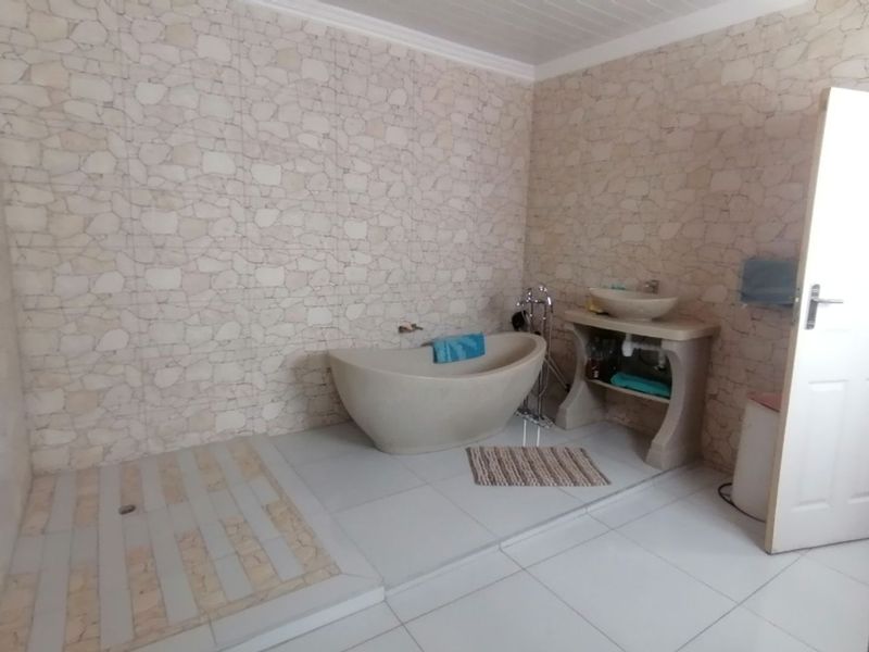 A bathroom featuring a freestanding stone-style bathtub, a raised shower area with tiled flooring, and a stone vanity with a vessel sink.