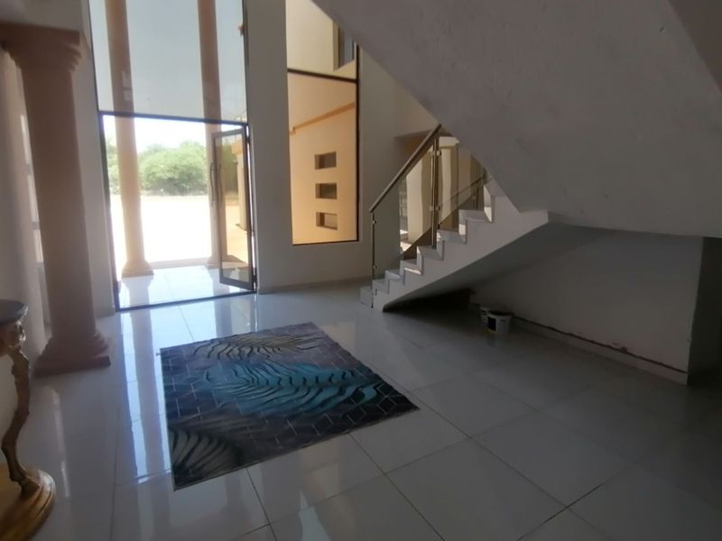 Spacious double-volume entrance hall featuring large glass windows, tiled flooring, and a modern staircase with glass balustrades.