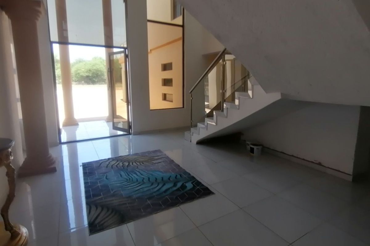 Spacious double-volume entrance hall featuring large glass windows, tiled flooring, and a modern staircase with glass balustrades.