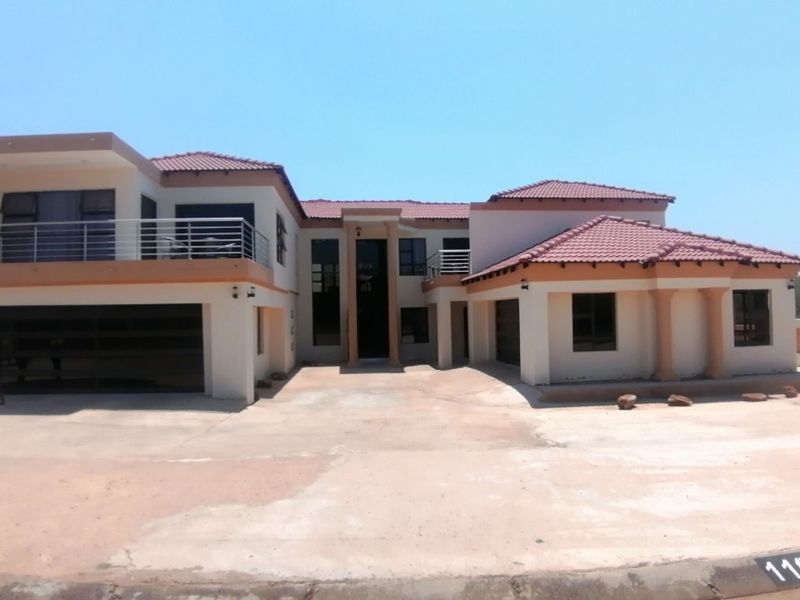 A large double-story residential property featuring a tiled roof, multiple balconies with metal railings, and an expansive concrete driveway.