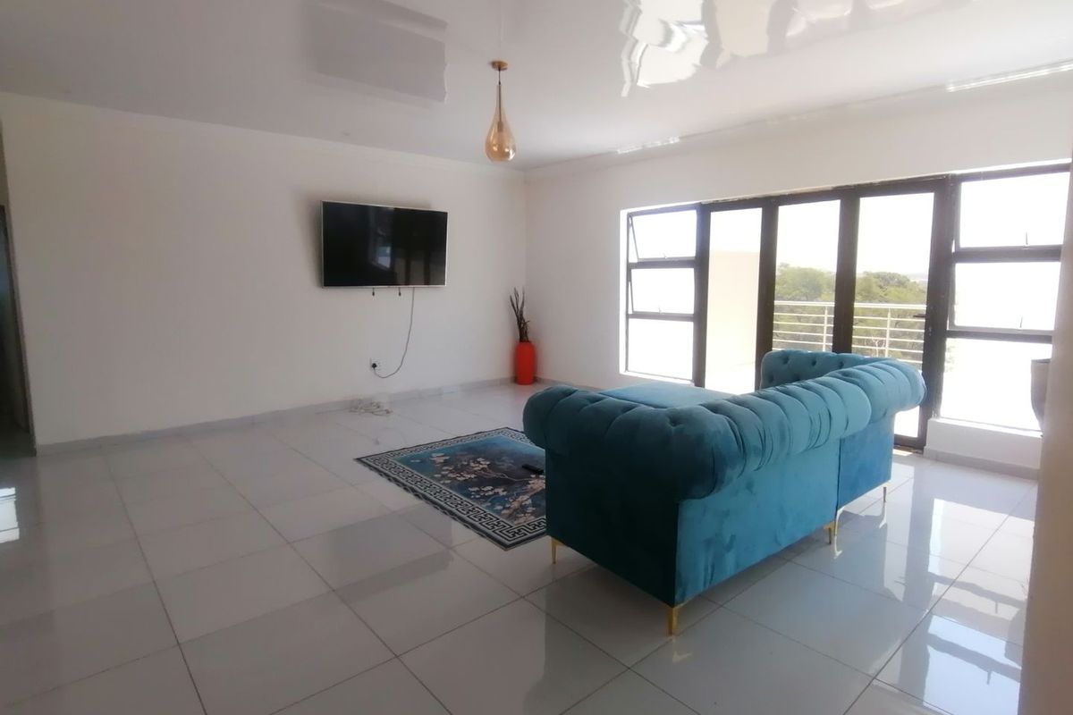 Spacious living area featuring large format floor tiles, a high-gloss ceiling, and expansive glass sliding doors leading to an outdoor balcony.