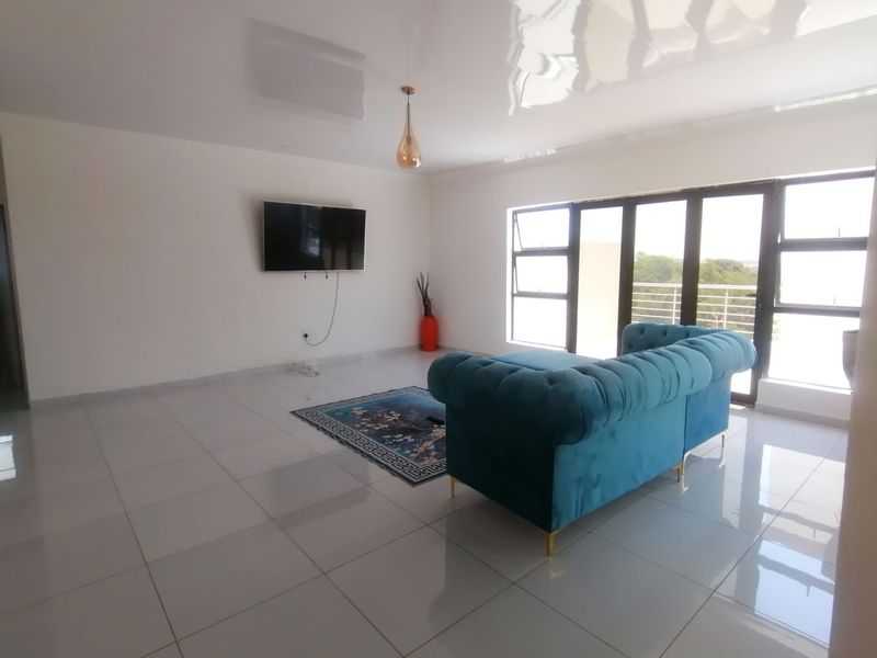 Spacious living area featuring large format floor tiles, a high-gloss ceiling, and expansive glass sliding doors leading to an outdoor balcony.