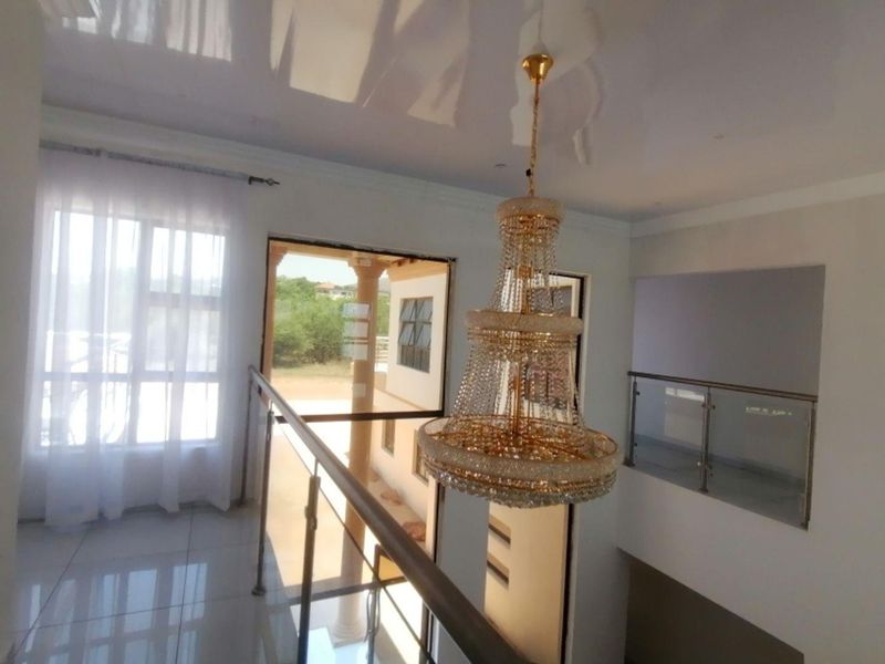 A bright landing area featuring a large crystal chandelier, polished tile flooring, and a modern glass balustrade overlooking the lower level.