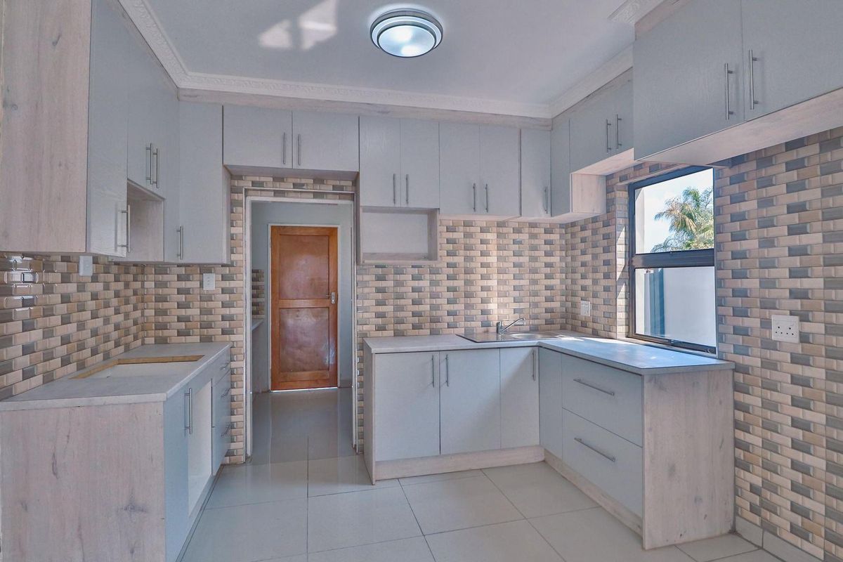 A modern kitchen featuring light-toned cabinetry, tiled backsplash, tiled flooring, and a stainless steel sink, offering a clean and functional workspace.