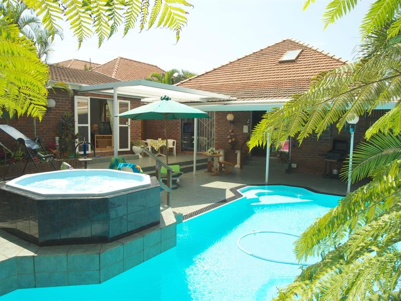 Outdoor entertainment area featuring a swimming pool, raised tiled jacuzzi, and a covered patio space with brick exterior finishes.