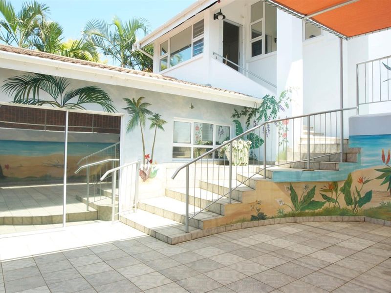 A paved outdoor patio area featuring a staircase with metal handrails, sliding glass doors, and decorative wall murals.