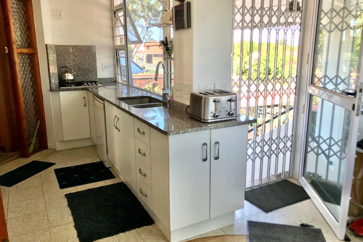 A functional kitchen featuring white cabinetry, granite countertops, a gas hob, and direct access to an outdoor area through a security gate.