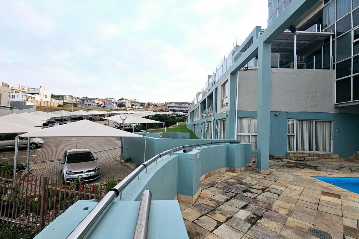 Exterior view of the apartment complex featuring a paved patio area, swimming pool, and adjacent covered parking facilities.