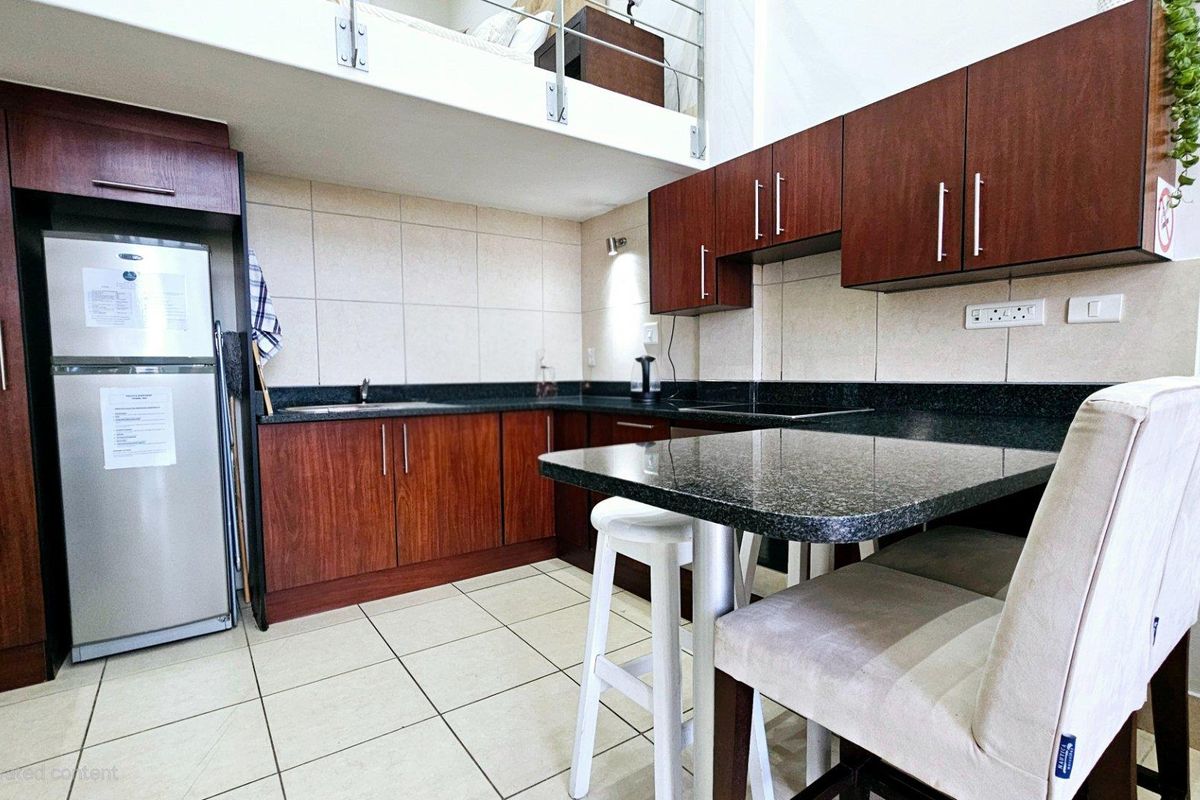 Compact kitchen featuring dark wood cabinetry, granite countertops, and a built-in breakfast bar, situated beneath a mezzanine level.