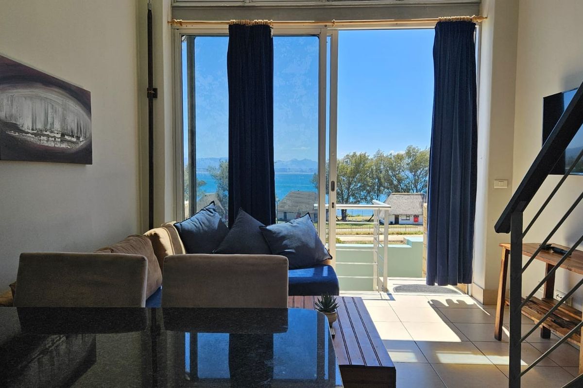 A bright living area featuring large sliding glass doors that open to a balcony with scenic coastal views and an internal staircase.