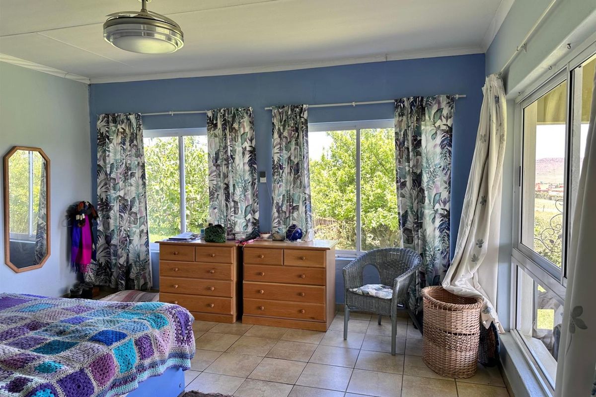 A bedroom featuring tiled flooring, a ceiling fan, and large sliding windows that provide natural light and garden views.