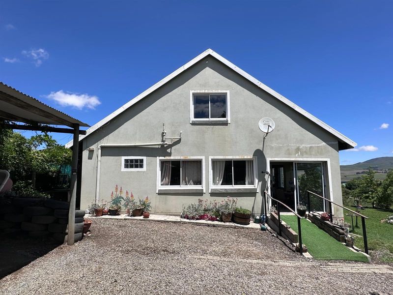 Rear elevation of the property featuring a gravel driveway, a ramp with handrails, and a covered outdoor structure.