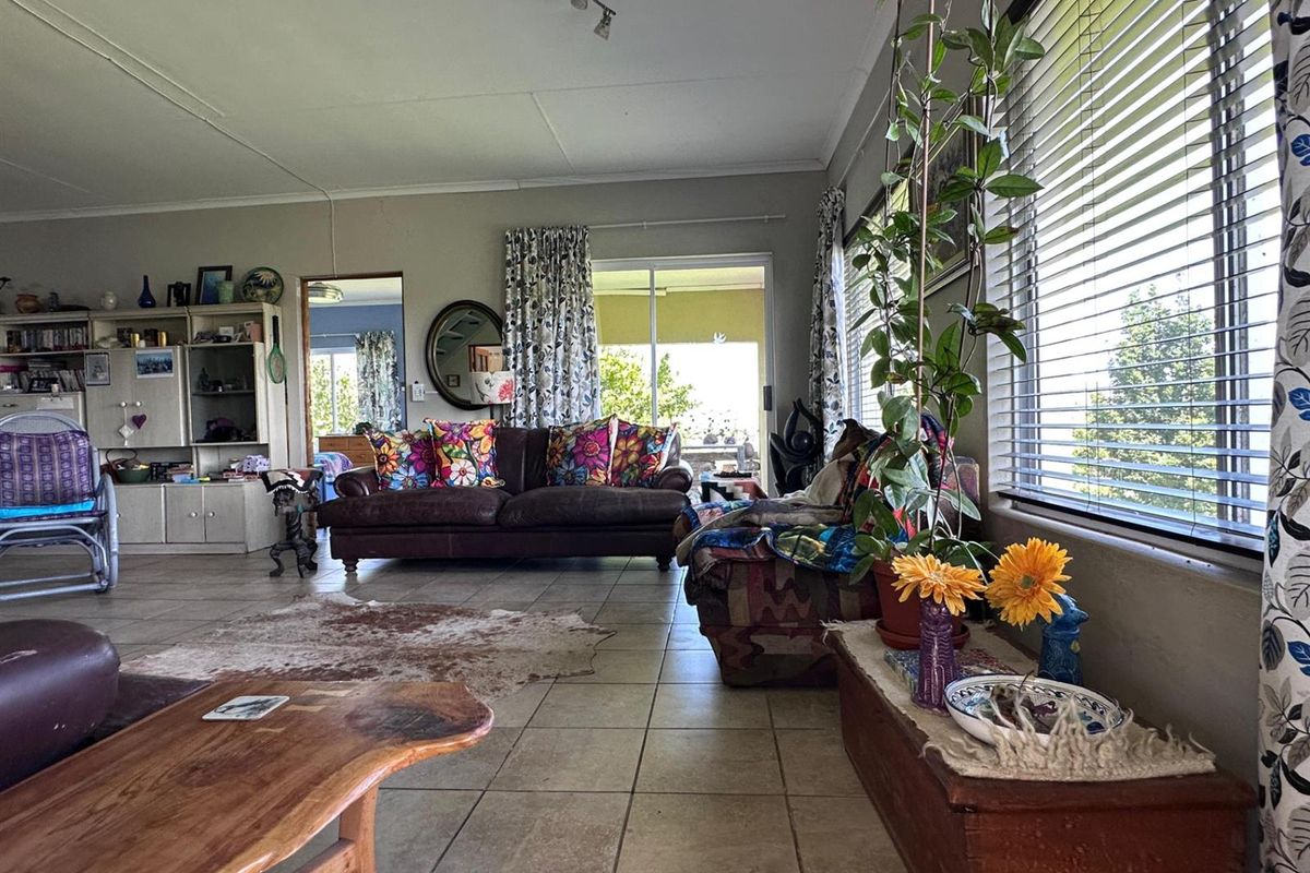 Spacious living room featuring tiled flooring, large windows with venetian blinds, and direct access to an outdoor patio area through sliding glass doors.