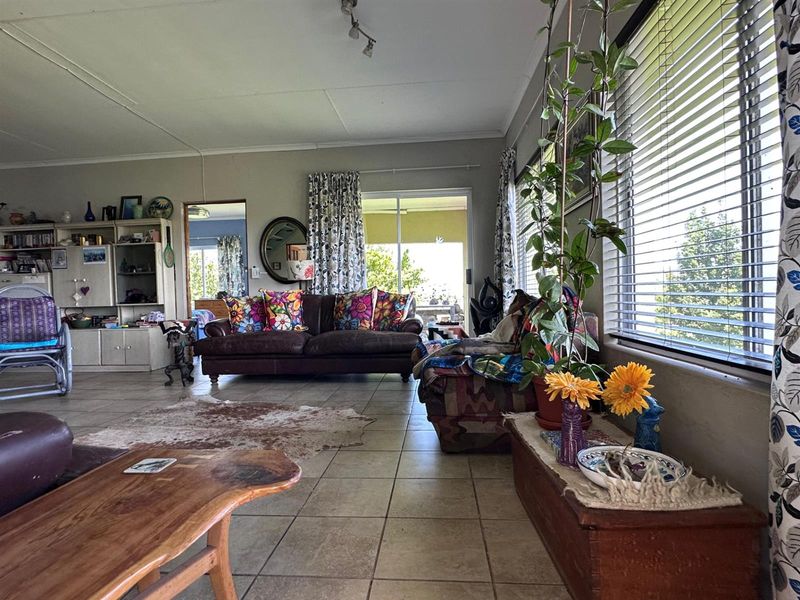 Spacious living room featuring tiled flooring, large windows with venetian blinds, and direct access to an outdoor patio area through sliding glass doors.
