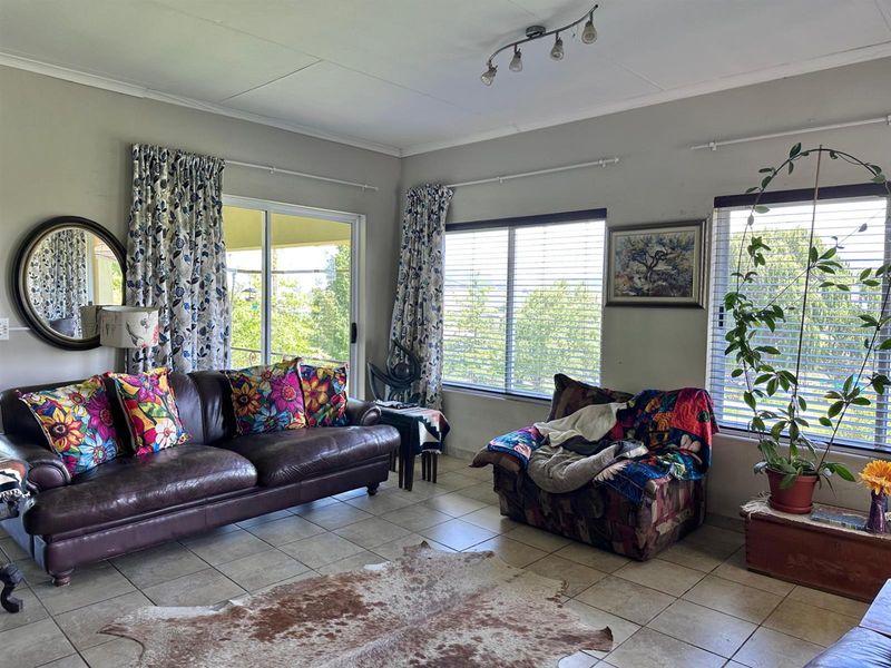 A bright living room featuring tiled flooring, track lighting, and large windows with access to an outdoor patio area.