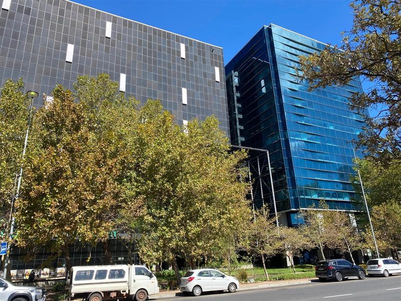 A modern multi-story commercial office building featuring a contemporary glass facade and dark metal cladding, situated along a street with mature trees.