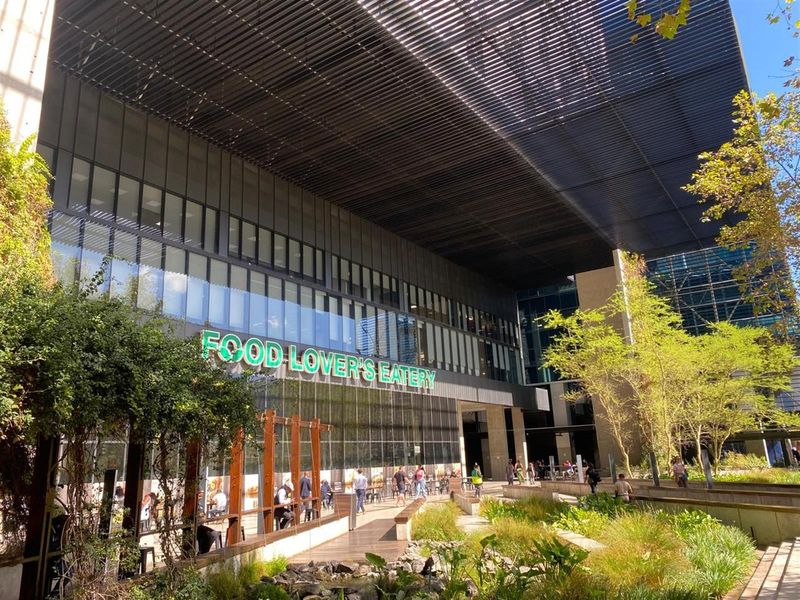 Modern commercial office building exterior featuring a large glass facade, extensive metal canopy, and well-maintained landscaped courtyard area.