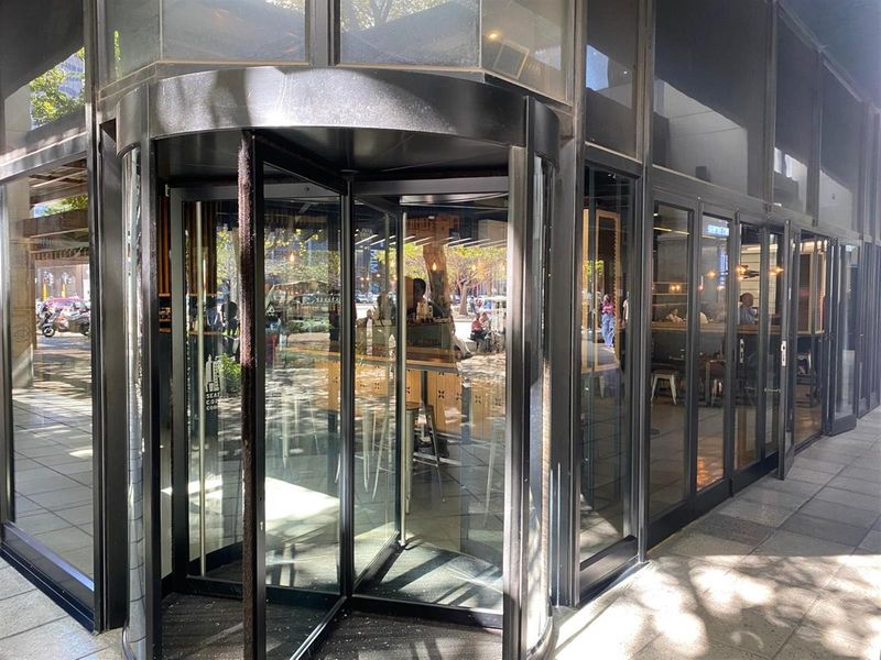 Modern office building entrance featuring a prominent revolving glass door and extensive floor-to-ceiling glass facade at street level.