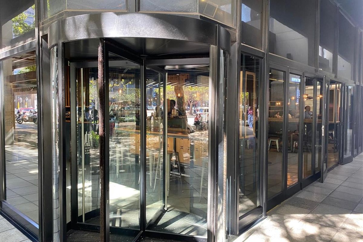 Modern office building entrance featuring a prominent revolving glass door and extensive floor-to-ceiling glass facade at street level.