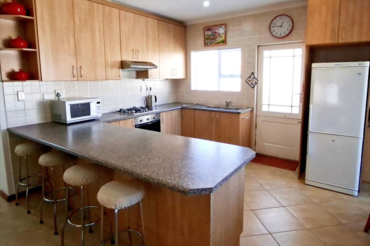 A functional kitchen featuring light wood cabinetry, a breakfast bar, tiled backsplash, and a built-in gas hob with an extractor fan.
