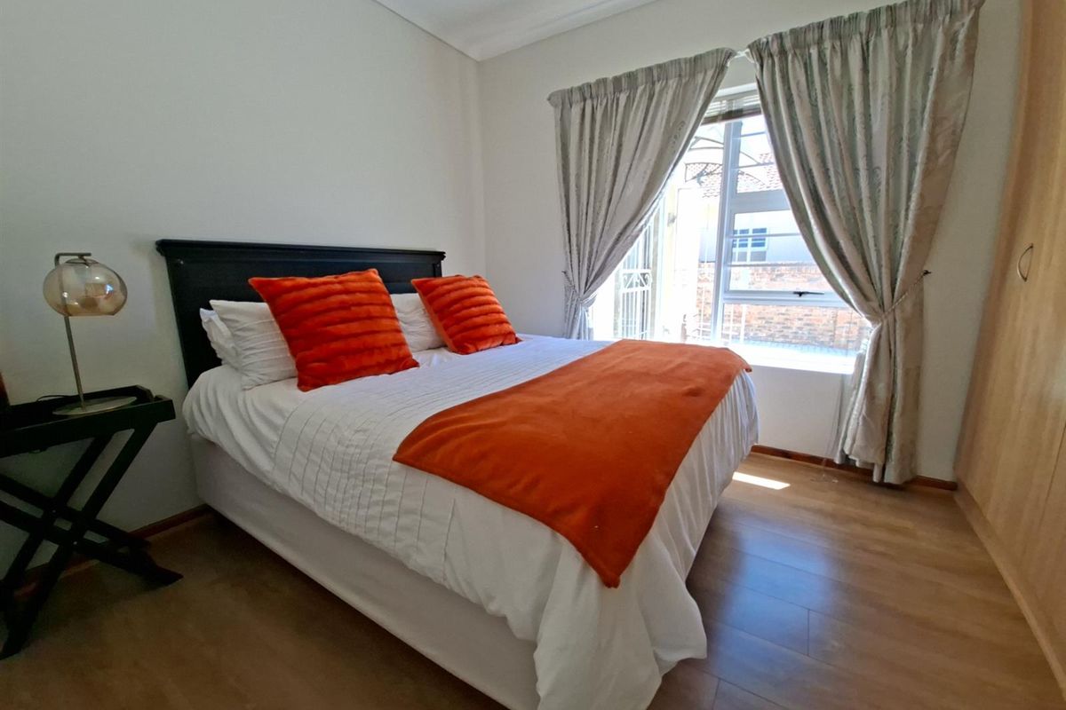 A well-maintained bedroom featuring laminate flooring, built-in cupboards, and a window with natural light.