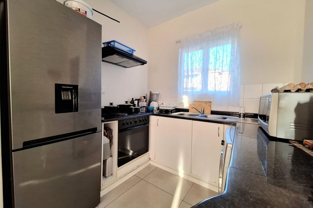 A functional kitchen featuring granite countertops, built-in oven, extractor fan, and tiled flooring with a window providing natural light.