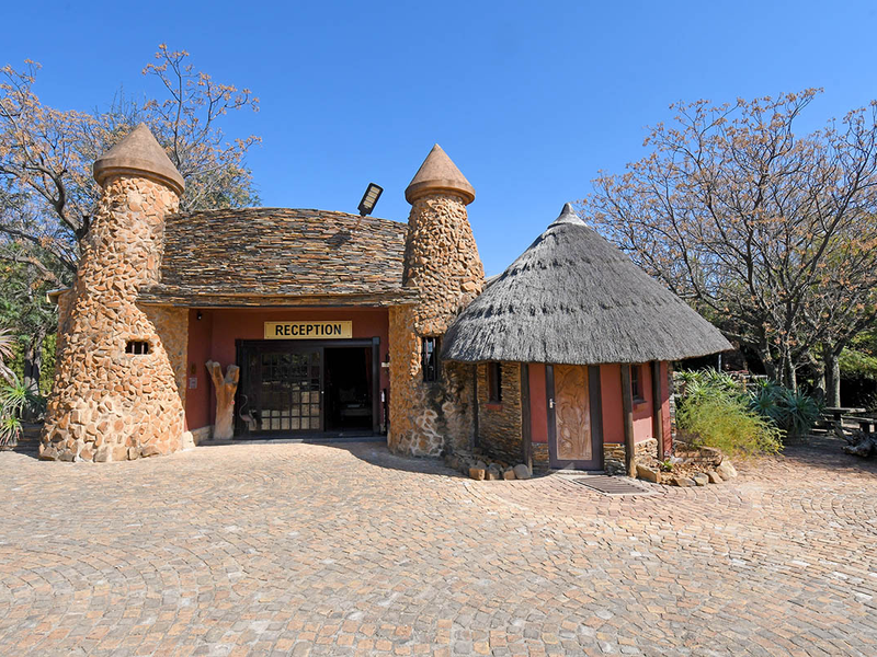 Front view of a lodge reception building featuring unique stone turret architecture, a traditional thatched roof, and a paved entrance area.